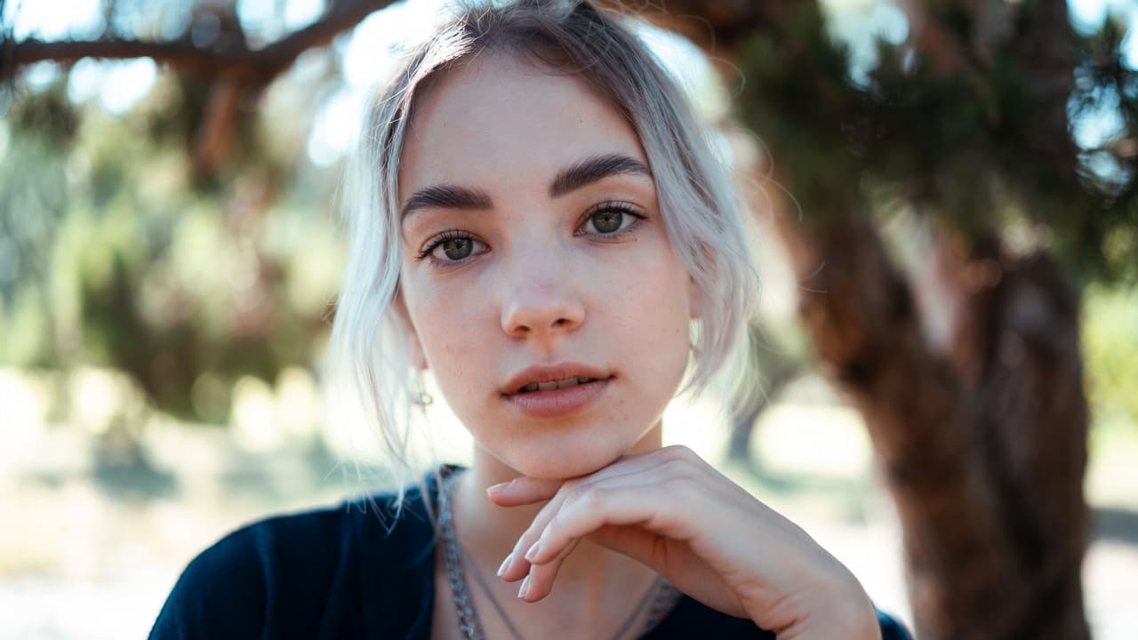 Close-up portrait of a silver-haired woman with green eyes, resting her chin on her hand.