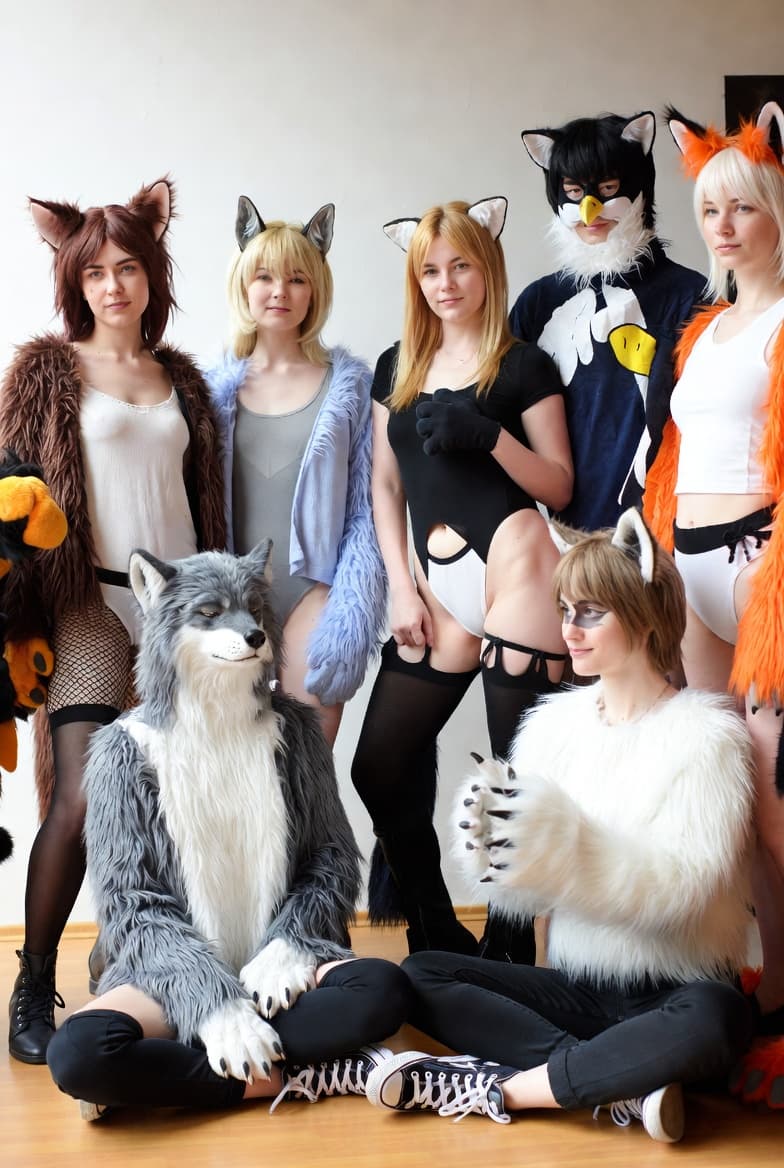 Seven people in animal-themed costumes and fursuits pose together against a plain white wall.